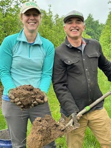 Two people in an orchard  holding scoops of healthy orchard soil